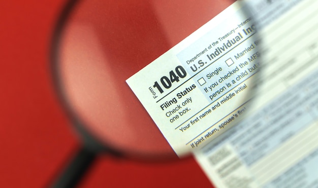 Photo tax season with magnifying glass, 1040 tax form background, red office desk top view photo