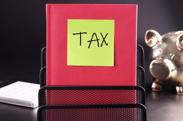 TAX text on a yellow sticker pasted on an upright diary on a black background