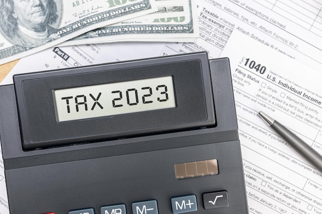 Фото Концепция налогового времени 2023 текст на экране калькулятора, текстовые формы и долларовые банкноты на столе вид сверху