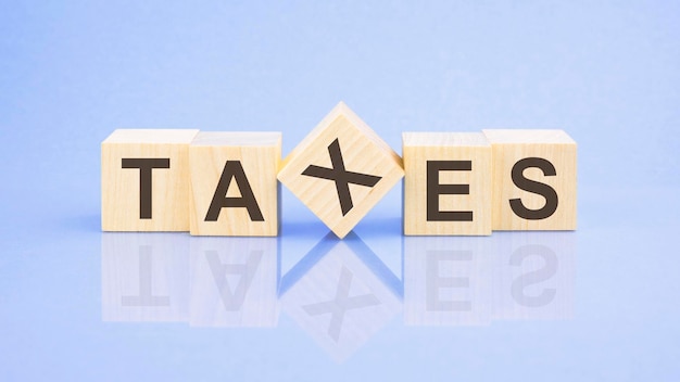 TAXES 단어는 나무 큐브 근접 촬영 밝은 파란색 배경 흰색 표면 테이블에 작성됩니다