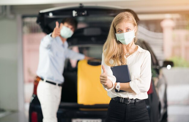 Foto il tassista con la maschera medica che mette valigie gialle di donne nel bagagliaio di un'auto