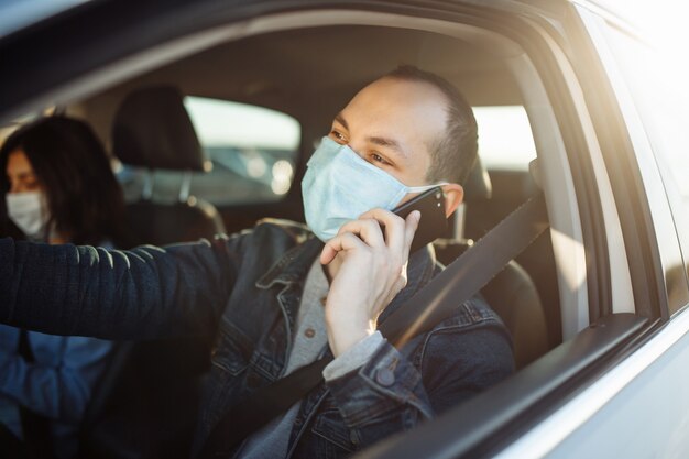 Taxi driver talking on the cell phone and wearing sterile
medical mask while waiting in a traffic during coronavirus
pandemic.