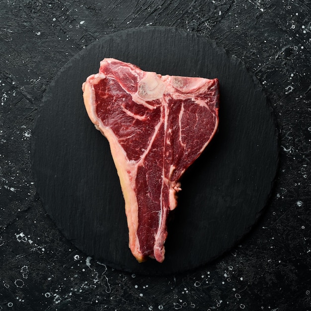 The tbone or porterhouse steak of beef aged steak top view on a\
black stone background