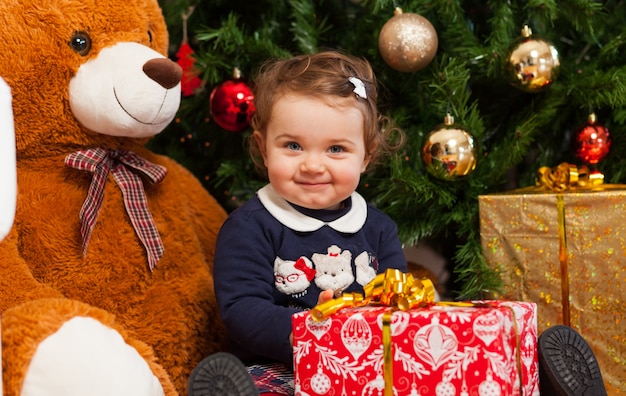 Tddler meisje met geschenken in de buurt van de kerstboom.