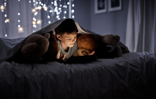 Te nieuwsgierig om te slapen Shot van een schattig jongetje dat 's nachts in bed een digitale tablet gebruikt