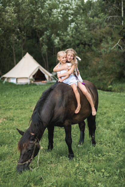 Te paard, twee kinderen meisjes, zussen, paardrijden buiten, glimlachend en knuffelen elkaar