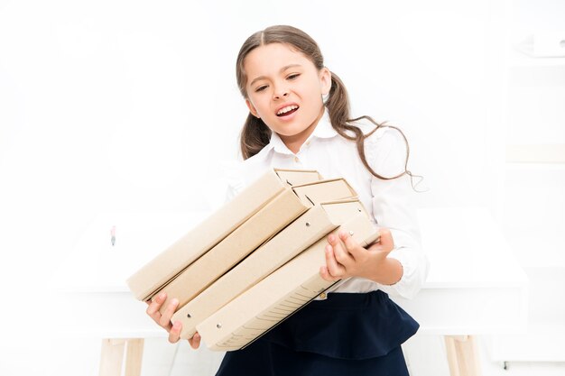 Te veel informatie. kind leert en studeert hard. terug naar school. boos meisje met werkmapmappen. Opleiding. zware documenten. Op weg naar kennis. klein meisje in schooluniform. veel huiswerk.