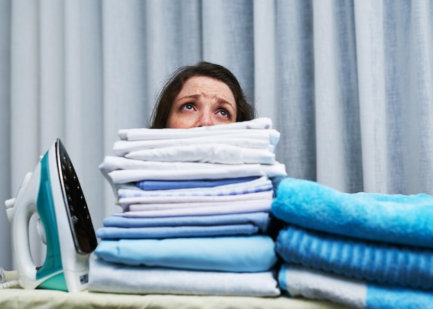 Te veel om te weinig tijd te doen Shot van een angstig kijkende jonge vrouw achter een stapel wasgoed op een strijkplank