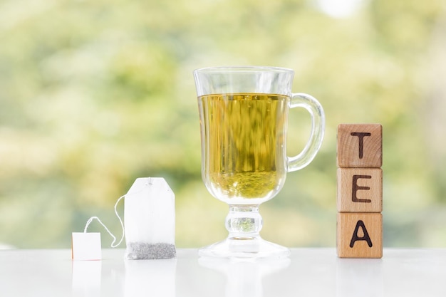 Photo tea bag and cup of tea on green summer background