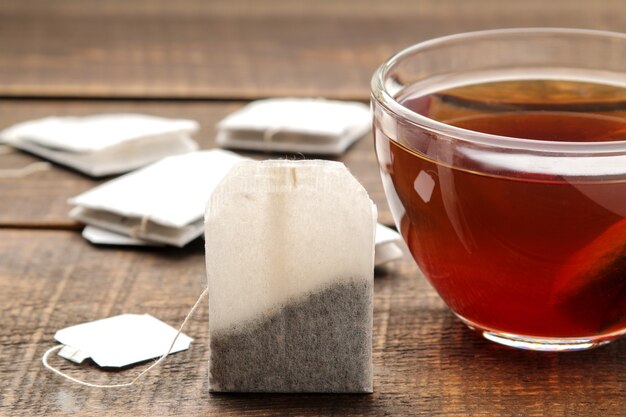 Фото Чайный пакетик в стеклянной чашке на коричневом деревянном фоне. заваривать чай