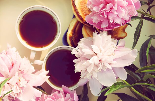 Tea in country style in summer garden in the village. Two cups of black tea on wooden tray and blooming peony flowers in sunlight.