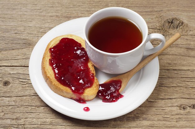 Tea cup and bread with jam in plate on old wooden table
