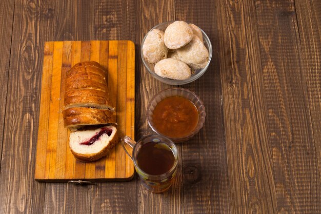 Tea in a cup, buns and jam and cutted   loaf are on the wood table