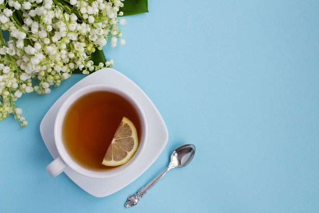 Tea in the cup and lilies of the valley on blue