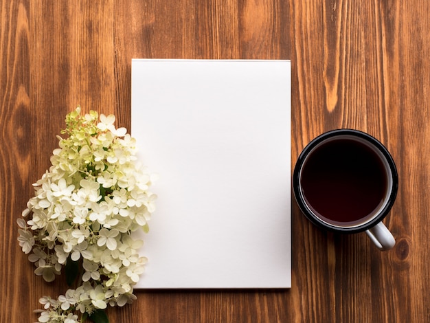 Tea cup, apri il blocco note con una pagina bianca pulita e un fiore bianco di ortensia