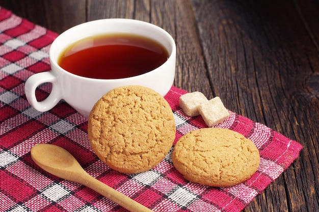 Photo tea cup with oatmeal cookie on dark wooden table covert red tablecloth