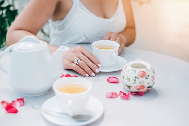 Tea cups and woman's hands holding one cup on table with rose petals