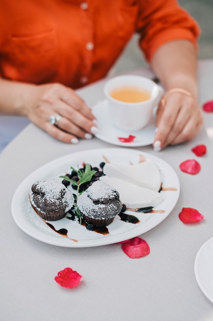 Tea cups and woman's hands holding one cup on table with rose petals