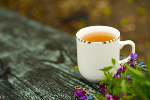 お茶と花庭の木製の机の上に白茶マグカップで熱いハーブティー