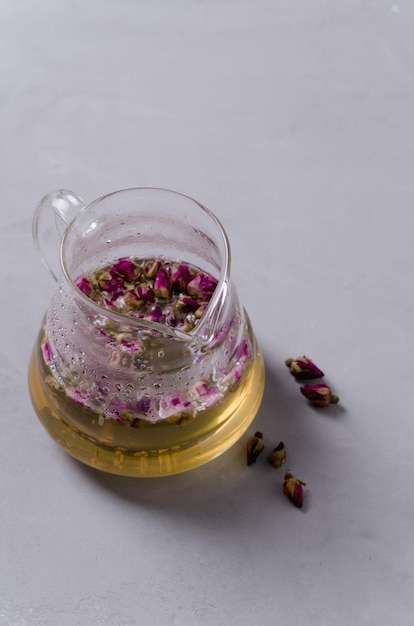 Tea from buds and rose petals A custard teapot with tea stands on a concrete gray background copying the space of the vertical background