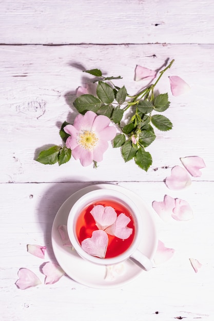 Tè dai fiori di rosa canina. bevanda vitaminica estiva, luce intensa, ombra scura. fondo in legno bianco, vista dall'alto