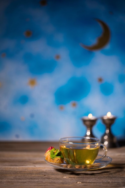 Tea in a glass cup with Arabic sweets on a wooden surface Night blue sky in the background