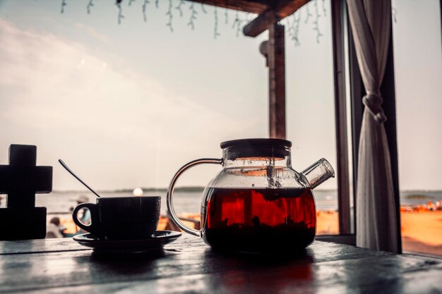 Tè in una teiera di vetro e una tazza su un tavolo di legno all'aperto brunch del caffè costiero