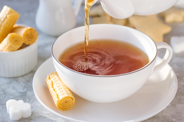 Tea is poured into a white mug of teapot. next to it are waffles and sugar on a platter