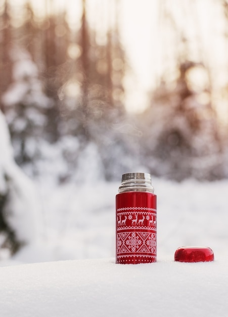 Tea in red thermos in winter forest