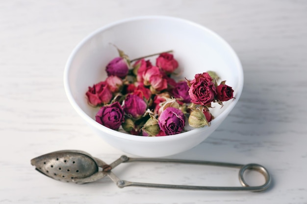 Tea rose in bowl on light wooden background