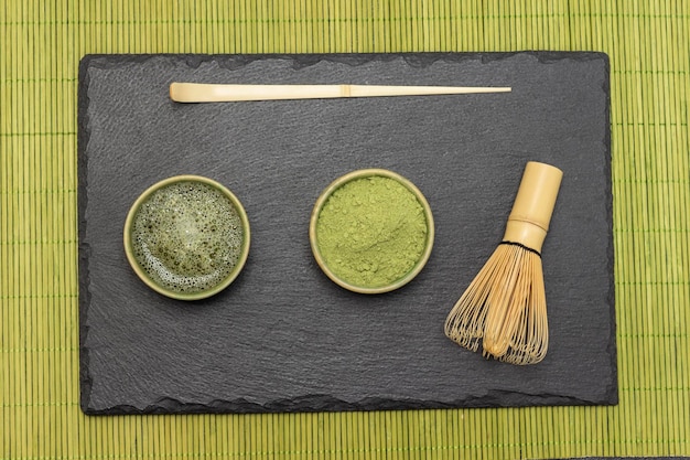 Tea spoon bamboo whisk matcha tea powder and matcha tea on stone board Flat lay Background of small green wooden sticks