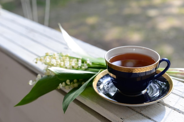 お茶と春の花庭の黒またはハーブティーとスズランの花の花束のカップ