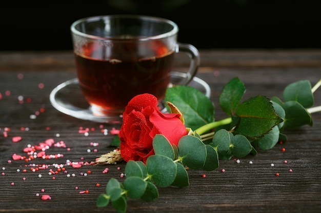 透明なカップに入ったお茶、色のキャンディー、濃い色の赤いバラ