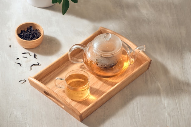 Tea in a transparent cup and teapot on a wooden background