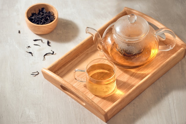 Tea in a transparent cup and teapot on a wooden background