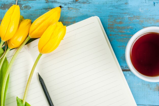 Tea, tulips and notebook on blue table