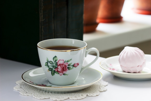 Foto tè in una tazza vintage, marshmallow su un piattino vintage e vecchi libri su uno sfondo chiaro.