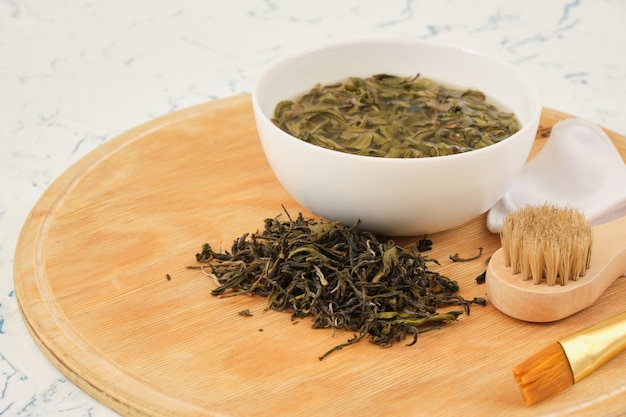 Tea water in a bowl and dry fermented tea leaves on a wooden tray light background natural cosmetics concept