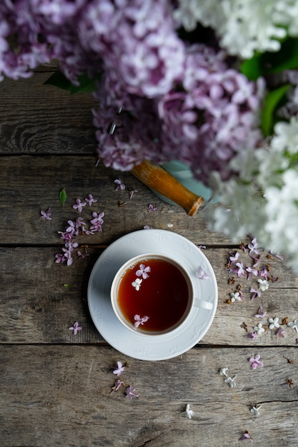 Tea in white tea cup, bouquet of lilac flowers on old wooden table