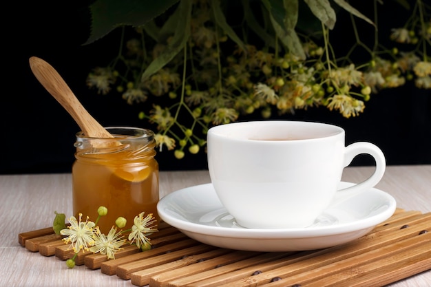 Tea in white with linden, honey jar and spoon on a bamboo stand