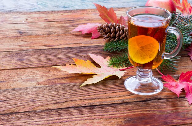 Tè con cannella e limone, mele mature, foglie di acero rosse di autunno, ramo di abete e pigne sul primo piano di legno della tavola