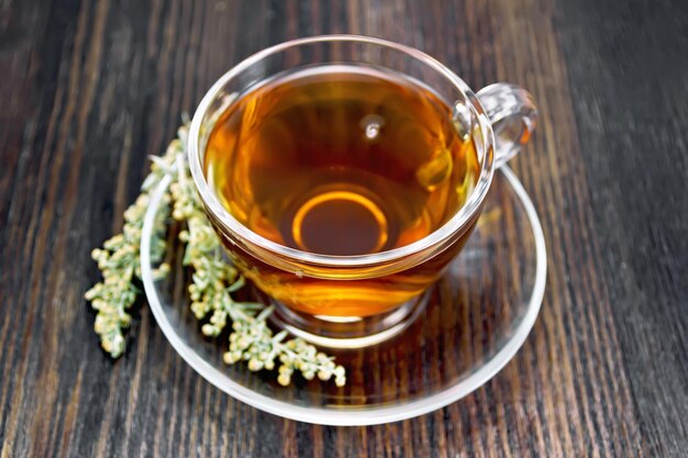 Tea with gray wormwood in glass cup on dark board