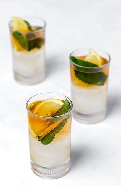 Tea with ice, mint and lemon wedges on white table