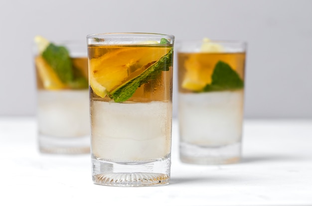 Tea with ice, mint and lemon wedges on white table