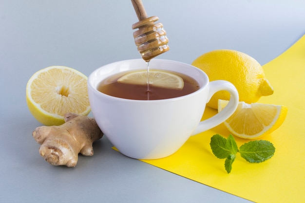 Foto tè con limone, miele e zenzero nella tazza bianca su sfondo giallo grigio. avvicinamento.