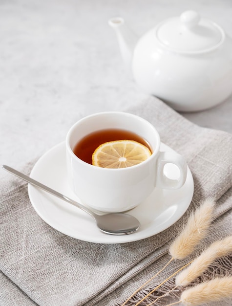 밝은 배경에 찻주전자가 있는 흰색 컵에 레몬을 넣은 차 건강하고 맛있는 아침 식사의 개념