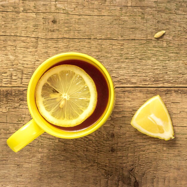 Tea with lemon in a yellow mug on a wooden background and fresh lemonTop view