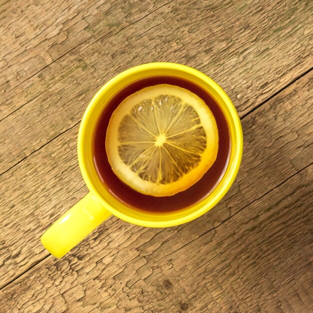 Tea with lemon in a yellow mug on a wooden background Top view