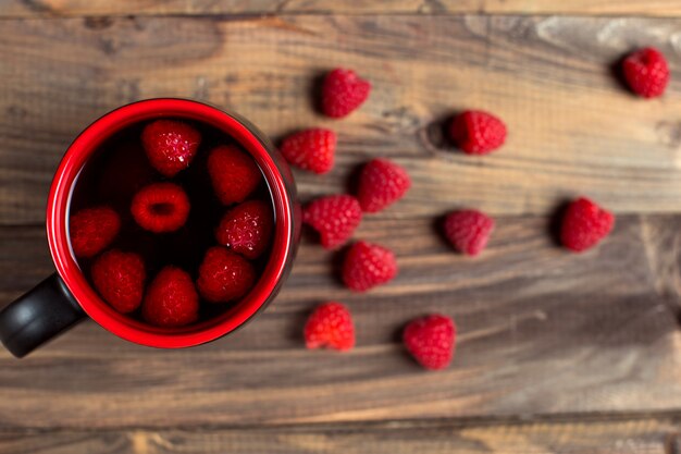 Tea with raspberries and berries next to a cup, on a wooden vintage table.