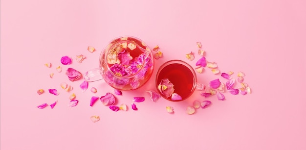 Tea with rose petals in glass teapot on pink background